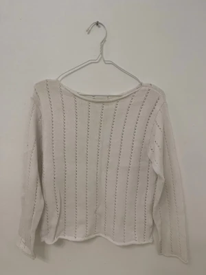 Vit stickad tröja med hålmönster - Säljer en vit stickad tröja med långa ärmar och dekorativa vertikala hålmönster. Tröjan har en rak passform och rund halsringning. Perfekt för dig som gillar en enkel men ändå detaljrik stil. Storlek 150 och passar dig med storlek XS/S