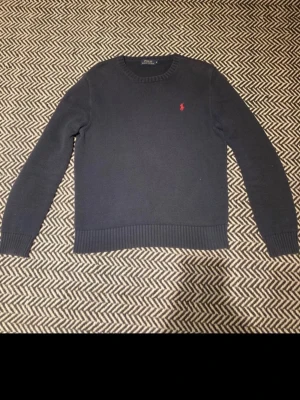  Ralph Lauren tröja  - Mörkblå stickad tröja från Polo Ralph Lauren med rund halsringning och röd broderad logga på bröstet. Tröjan har ribbstickade muddar vid ärmslut och nederkant. Perfekt för en stilren och klassisk look. Bara att skriva vid frågor!