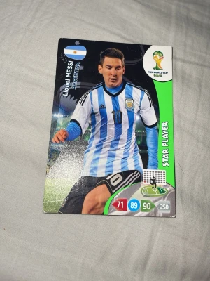 FIFA World Cup spelkort Argentina - Samlarspelkort från Panini med motiv av en argentinsk fotbollsspelare i blåvit randig tröja, nummer 10. Kortet har gröna och svarta detaljer samt FIFA World Cup Brasil-logga. Perfekt till samlare av fotbollskort.
