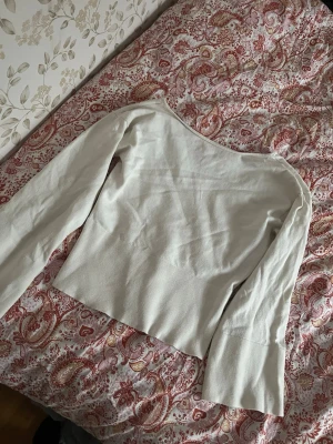 Vit långärmad topp med bred kant - Säljer en stilren vit topp med lång ärm och bred kant nedtill från ginatricot Toppen har en enkel, rak passform och är tillverkad i ett mjukt material som känns bekvämt mot huden. Perfekt att matcha med jeans eller kjol för en clean look. Och tröjan är öppen i ryggen.storlek 170