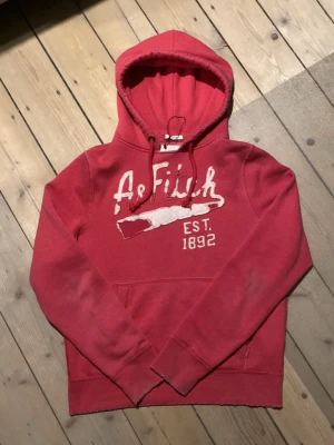 2000s Abercrombie & fitch hoodie - Står XXL men sitter som en L. Snygg röd hoodie från Abercrombie & Fitch med broderad logga och texten 'EST. 1892' på bröstet. Klassisk känguruficka framtill och justerbar huva med dragsko. Perfekt för en avslappnad och trendig stil.