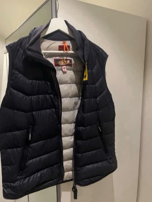 Mörkblå dunväst från Parajumpers - Snygg mörkblå dunväst från Parajumpers med quiltad design och dragkedja framtill. Insidan är ljusgrå och västen har hög krage samt två sidofickor med dragkedja. Perfekt för lager-på-lager och streetwear-vibe. Jag är 175cm och västen är perfekt på mig. Bra skick 