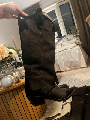 ZARA Svarta höga cowboy boots - Säljer ett par svarta höga cowboy boots med klassiska broderade detaljer och spetsig tå. Skorna har en markerad klack och är tillverkade i mockaliknande material. 