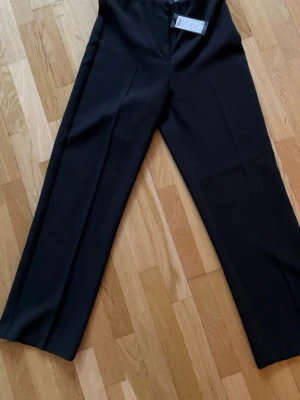 Svarta kostymbyxor Vero Moda S - Snygga svarta kostymbyxor från Vero Moda, modell VMSANDY HR Straight Ankle Pant. Byxorna har rak passform, hög midja och ankellängd. Perfekta till en stilren look och tillverkade i ett mjukt, vävt material. Innerbenlängd 75 cm. Prislapp kvar