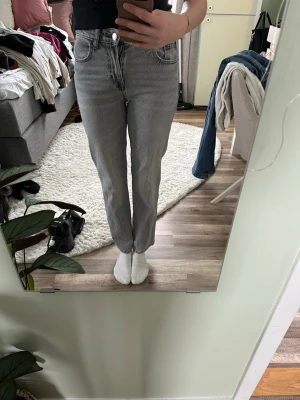  Jeans  - Säljer ett par ljusgrå jeans med rak passform och hög midja. Klassisk femficksmodell med dragkedja och knapp framtill. Jeansen har en avslappnad look och är perfekta till en enkel t-shirt eller hoodie. Materialet är denim i bomull.