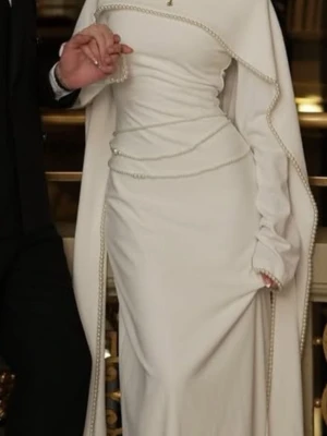 Vit maxiklänning med pärldetaljer från Khanum's london - Elegant vit maxiklänning med figurnära passform och långa ärmar. Klänningen har unika pärldetaljer längs kanterna och en cape-liknande axelparti som ger en lyxig känsla.  original price: 3600