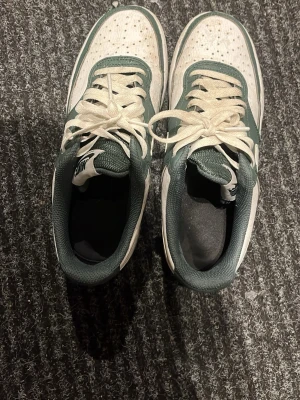 Nike Dunk Low grön/vit sneaker - Snygga Nike Dunk Low sneakers i grönt och vitt läder med klassisk swoosh på sidan. Lågt skaft, vita skosnören och perforerad tåbox för extra ventilation. Perfekta för dig som gillar streetwear och vill ha en stilren look.