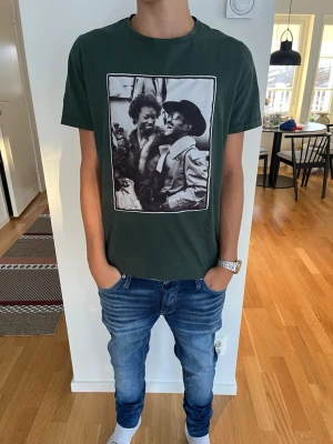 Grön t-shirt med tryck från Limitato - Cool grön t-shirt från Limitato med ett stort svartvitt fototryck på bröstet. T-shirten har rund hals och korta ärmar. Perfekt för dig som vill sticka ut med en unik design och konstnärlig vibe.