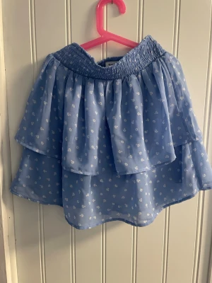 Blå kort kjol från kappbahl - Säljer en blå kjol med vita blommotiv. Storlek 158-164. Köpt från kappbahl. Kontakta om du är intresserad!