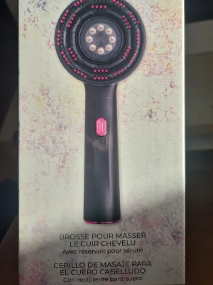 Hårbottens Massageborste Med behållare för serum Svart massageborste för hårbotten Med Infrarött ljus - Elektrisk hårborste i svart plast med rosa detaljer och metallpiggar, designad för att massera hårbotten. Borsten har ett inbyggt serumreservoar och ett rosa knappreglage på handtaget. Perfekt för dig som vill boosta hårvårdsrutinen med massage. Med Infrarött ljus. Olika hastighet på borsten 