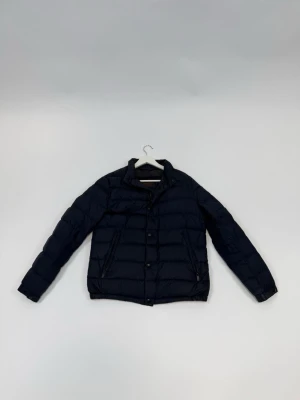 Massimo Dutti Mörkblå pufferjacka  - Fet mörkblå pufferjacka från Massimo Dutti. Jackan har hög krage och stängs med båda dragkedja och knappar. Perfekt för kalla dagar och ger en clean look.