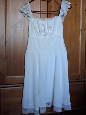 Vit klänning med spetsdetaljer - Söt vit klänning med spets på axelbanden och nederkanten. Klänningen har en luftig passform och är ärmlös med romantiska spetsdetaljer som ger en feminin känsla. Perfekt för varma dagar eller speciella tillfällen.                                        Hittar ingen storlek men passar mig med storlek 36-38. Fint skick!