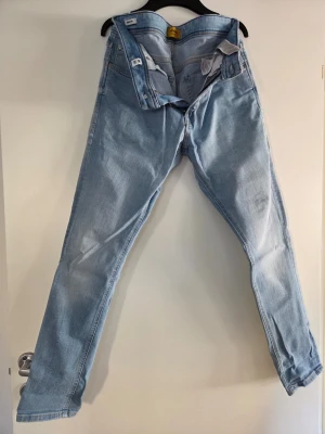 Ljusblå jeans från Nudie Jeans - Säljer ett par ljusblå jeans från Nudie Jeans med klassisk femficksdesign och raka ben. Jeansen har snygga detaljer på bakfickorna och är tillverkade i bomull. Perfekt för dig som gillar en avslappnad och trendig look.