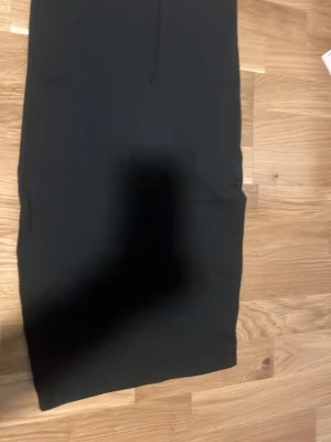 Svart långkjol från Gina Tricot - En stilren svart långkjol från Gina Tricot i storlek S. Kjolen har en rak och enkel design med elastisk midja och är tillverkad i ett mjukt syntetmaterial som ger en skön passform. Perfekt för dig som gillar minimalistisk stil.