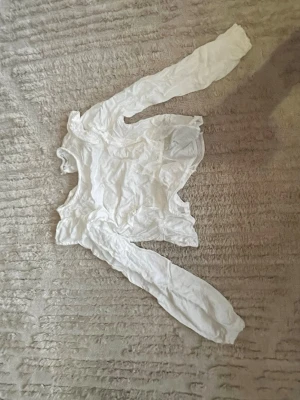 Vit långärmad blus med volang - Säljer en vit blus med långa ärmar och volangdetaljer. Blusen har en feminin och luftig design som passar perfekt till jeans eller kjol. Materialet känns lätt och bekvämt, och volangen ger en extra touch till looken.