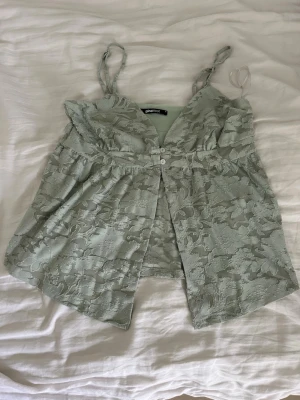 Ljusgrön spetsblus från Gina Tricot - Säljer en ljusgrön blus från Gina Tricot med vackert spetsmaterial och knappar framtill. Blusen har smala axelband och ett lätt utställt fall. Perfekt för dig som gillar romantiska detaljer och en feminin look. Färgen är lite mörkare på dem första bilderna men sista bilden är i dagsljus, använt en gång💐🫶