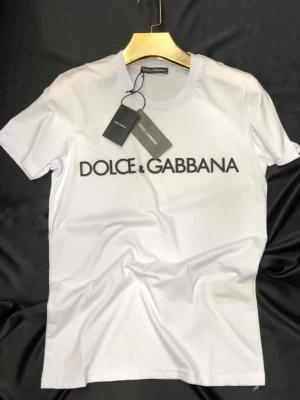 Vit Dolce & Gabbana t-shirt - Snygg vit t-shirt från Dolce & Gabbana med klassisk logga tryckt framtill. T-shirten har rund halsringning och korta ärmar, perfekt för en clean och stilren look. Tillverkad i mjuk bomull för maximal komfort.