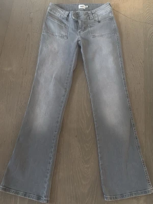 Grå bootcut jeans med fickor - Snygga grå bootcut jeans med utsvängda ben och stora framfickor. Jeansen har klassiska bakfickor och en cool tvättad look. Perfekta för dig som gillar en avslappnad men trendig stil. Midjemått ca 35 cm. innebenslängd ca 74 cm
