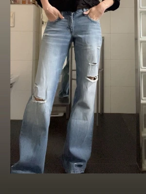 Ljusblåa slitna jeans med raka ben - Säljer ett par ljusblå jeans med raka ben och flera slitningar på framsidan. Jeansen har klassisk femficksdesign och är tillverkade i denim. Perfekt för dig som gillar en avslappnad och trendig look.