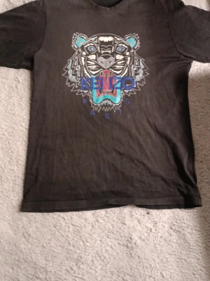 Svart Kenzo t-shirt med tigertryckk - Cool svart t-shirt från Kenzo med ikoniskt tigertryck och färgglada detaljer framtill. Klassisk passform och rund halsringning. Perfekt för dig som vill sticka ut med en statement-tee från ett välkänt märke.