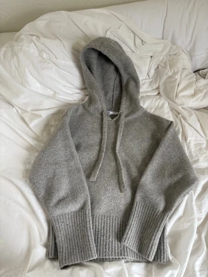 Grå hoodie med ribbade detaljer - Mjuk grå hoodie från zara med breda ribbade muddar vid ärmslut och nederkant. Tröjan har en stor huva med dragsnören och är tillverkad i ett stickat material. Perfekt blandning mellan snygg o mysig tröja 