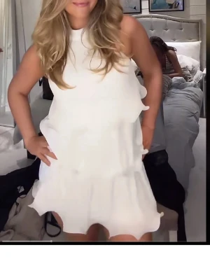 Vit student  volangklänning - Andvänd 1 gång på min student , Säljer en superfin vit kortklänning med volangdetaljer och hög hals. Klänningen är ärmlös och har en lös passform som ger en luftig och trendig look. Perfekt för sommarens alla tillfällen. Materialet känns lätt och bekvämt.