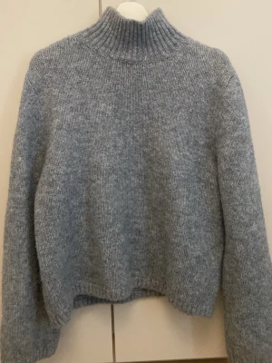 Ljusgrå stickad polotröja H&M - Mysig ljusgrå stickad tröja från H&M med en högre krage. Passar även personer i storlek M vid en mer oversized fit men även L då den är strechig. Kommer från ett djur och rökfritt hem!
