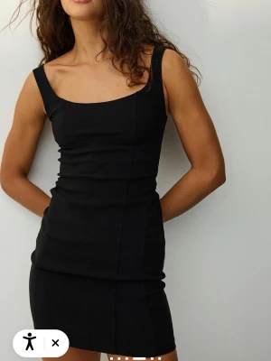 Svart kort klänning med breda axelband - En svart, tight och kort klänning med breda axelband och justerbar rygg. Klänningen har en enkel och stilren design med markerade sömmar och en rak halsringning. Perfekt för dig som gillar minimalistisk stil. Aldrig använd 