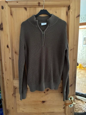 Brun stickad tröja med halvzip Grunt - Säljer en brun stickad tröja från Grunt i storlek L. Tröjan har en hög krage med halvzip och ribbstickade muddar vid ärmslut och nederkant. Perfekt för lager på lager och en avslappnad stil.