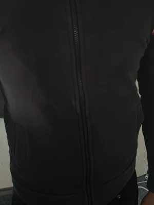 Mörkblå hoodie från Moncler - Snygg svart hoodie från Moncler med dragkedja framtill och fickor på sidorna. Ärmen har Monclers klassiska logga och ränder i vitt och rött. Perfekt för dig som gillar stilrena och exklusiva plagg. Materialet känns mjukt och bekvämt.