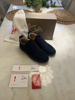 Christian Louboutin  - Upptäck tidlös elegans med dessa mörkblå skor från Christian Louboutin. Den djupa marinblå nyansen ger ett sofistikerat uttryck som passar lika bra till formella tillfällen som till en uppklädd vardagslook.  Designen är ren och minimalistisk, vilket låter materialets kvalitet och den ikoniska siluetten stå i fokus. Skorna är tillverkade i noggrant utvalt läder med en mjuk finish som ger både komfort och en exklusiv känsla. Den klassiska röda sulan tillför en subtil men igenkännbar signatur.