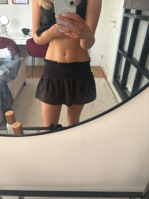 Svart volangkjol med smock - Kort svart kjol med bred smock i midjan och volang nedtill. Kjolen har en enkel och stilren look som har klippts kortare, men inget man ser utanpå! Passar perfekt till sommaren. Materialet känns lätt och flowy, vilket gör den skön att bära varma dagar.