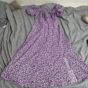 Lila blommig långklänning med puffärm - Superfin lila långklänning från Shein med vita blommor, puffiga kortärmar och smock i ryggen. Klänningen har slits framtill och resår vid axlarna så den kan bäras offshoulder. Perfekt för sommarens alla tillfällen!