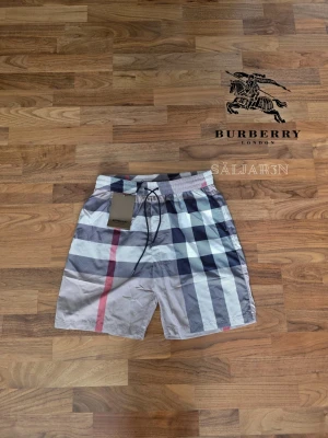 Burberry Shorts - 🩳 Burberry Shorts – Storlek M 🩳 Stilrena Burberry shorts med klassiskt rutmönster, perfekta för sommar, strand eller avslappnad vardag. Elastisk midja med justerbar dragsko ger bekväm passform. Tillverkade i lätt och slitstarkt material med mjuk känsla mot huden. Praktiska fickor för småsaker och Burberry-logga på detaljerna ger en lyxig finish. Shortsarna är i nyskick. 📦 Snabb leverans – Kontakta för frågor!