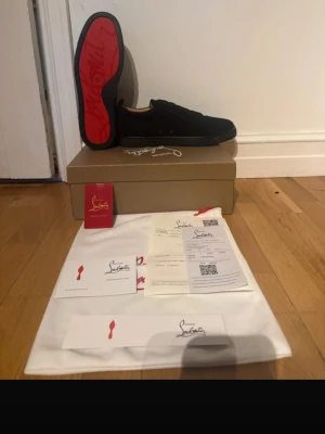Svarta sneakers från Christian Louboutin - Snygga svarta sneakers från Christian Louboutin med ikonisk röd sula och diskret logga på sidan. Skorna har en låg profil och är tillverkade i ett lyxigt material som ger en exklusiv känsla. Perfekt för dig som vill sticka ut med stil.