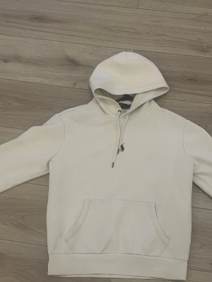 Vit hoodie från Polo Ralph Lauren - Snygg vit hoodie från Polo Ralph Lauren med klassisk huva och dragsko. Har en känguruficka framtill och den ikoniska lilla broderade hästloggan på bröstet. Tillverkad i mjukt bomullsmaterial som känns skönt mot huden. Perfekt för en avslappnad och stilren look.