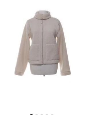 Beige teddyjacka med dragkedja - Mysig beige teddyjacka med hög krage och två stora fickor framtill. Jackan har rak passform och stängs med dragkedja. Perfekt för kyliga dagar när du vill vara både varm och snygg.