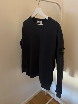 Mörkblå sweatshirt från Stone Island - Säljer en mörkblå sweatshirt från Stone Island med klassisk rund hals och lång ärm. Tröjan har den ikoniska logotypen på vänster ärm och är tillverkad i mjuk bomull. Perfekt för en avslappnad och stilren look.