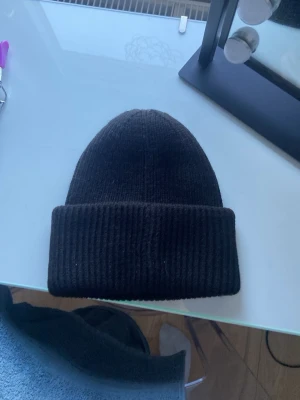 Svart ribbad mössa från Fairfield - Säljer en svart ribbstickad mössa från Fairfield Equestrian. Mössan är tillverkad i 100% akryl och har en bred uppvikt kant för extra stil och värme. Enkel och klassisk design som passar till det mesta.