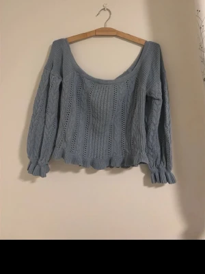 Ljusblå stickad tröja off-shoulder - Säljer en ljusblå stickad tröja med bred, rund urringning och långa ärmar. Tröjan har ett fint kabelstickat mönster och volangkant nedtill samt vid ärmslut, sitter off-shoulder.