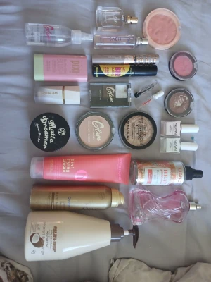 Smink- och basprodukter mix - Några är sönder, därav priset🥰 Ett kit med flera basprodukter för ansikte, inklusive foundation, highlighter, setting powder, blush, primer och ansiktskräm. Flera märken som Pixi, HEGLAM, W7 och L'Oréal. Färgerna går i ljusa och neutrala toner, med inslag av rosa och guld. Innehåller både puder och flytande produkter.