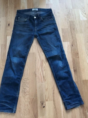Mörkblå jeans från Acne Studios - Snygga mörkblå jeans från Acne Studios med klassisk femficksdesign och raka ben. Jeansen har silverfärgade detaljer och subtila slitningar för en cool look. Perfekta för dig som gillar stilrena och trendiga jeans.