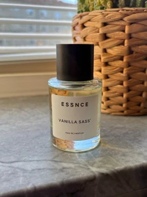 ESSNCE Vanilla Sass Eau de Parfum - ESSNCE Vanilla Sass Eau de Parfum är en parfym med en transparent glasflaska och svart cylinderformad kork. Doften har vaniljtoner och flaskan har en stilren vit etikett med svart text. Perfekt för dig som gillar söta och fräscha dofter. Sprutad några gånger. 