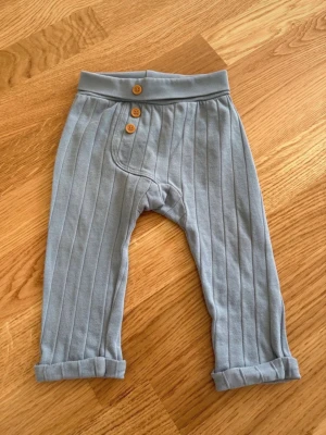 Bebisbyxor Fixoni stl 74 - Ljusblåa ribbade byxor från Fixoni i storlek 74.  I mycket bra skick, endast använda 1 gång.  100% bomull.   Från djur- och rökfritt hem.  Tvättat med parfymfritt tvättmedel, inget sköljmedel. ☺️