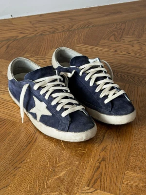 Mörkblå Converse One Star sneakers - Mörkblå Golden Goose sneakers i mocka med vit stjärndetalj på sidan och vita skosnören. Klassisk låg modell med vit sula och retrovibbar. Perfekta för dig som gillar streetstyle och vill ha en ikonisk sneaker i garderoben. 