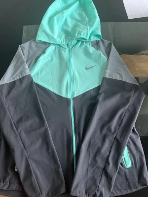 Nike hoodie i mintgrön och grå - Snygg hoodie från Nike i mintgrönt och olika nyanser av grått. Dragkedja framtill, huva och fickor på sidorna. Perfekt för en sportig och avslappnad stil. Tillverkad i mjukt och bekvämt material som passar året runt.