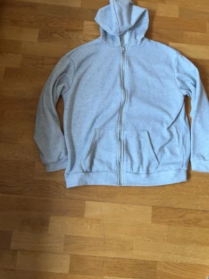 Ljusgrå hoodie med dragkedja SHEIN - Ljusgrå hoodie från SHEIN med dragkedja framtill och två fickor. Mjuk insida och klassisk huva. Perfekt för en avslappnad stil och enkel att matcha med andra plagg. Materialet är bomullsblandning för extra komfort.