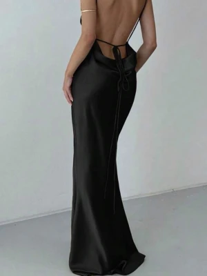 Svart långklänning i satin med öppen rygg - Elegant svart långklänning i satin med smala axelband och öppen rygg med snygg knytning. Klänningen har en figurnära passform och faller snyggt längs kroppen. Perfekt för dig som vill ha en stilren och sofistikerad look. Aldrig använd 