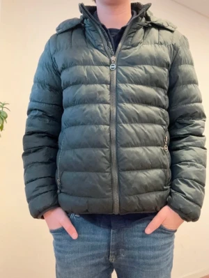 Mörkgrön dunjacka från Colmar - Snygg mörkgrön dunjacka från Colmar med quiltad design och hög krage. Jackan har dragkedja framtill, två sidofickor med dragkedja och Colmar-logga på ärmen. Perfekt för kalla vinterdagar och riktigt skön att bära.