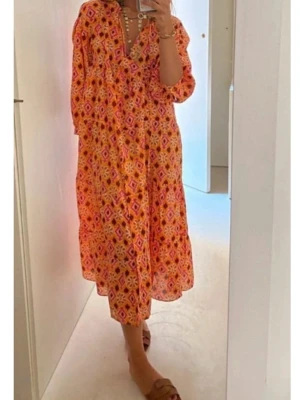 Mönstrad långklänning i orange och rosa - Färgglad långklänning med geometriskt mönster i orange, rosa och gula toner. Klänningen har v-ringning, trekvartsärm och en lös, flowy passform. Perfekt för varma dagar och somriga vibes.